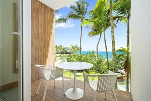 A balcony with a white table and chairs, overlooking a pool and palm trees, with a view of the ocean. - Beachfront Luxury Studio • Ultravioleta Cabarete (Cabarete)