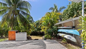 A paved pathway leading to a building with kayaks stored on a wall. - Fare Manava (Tiahura)