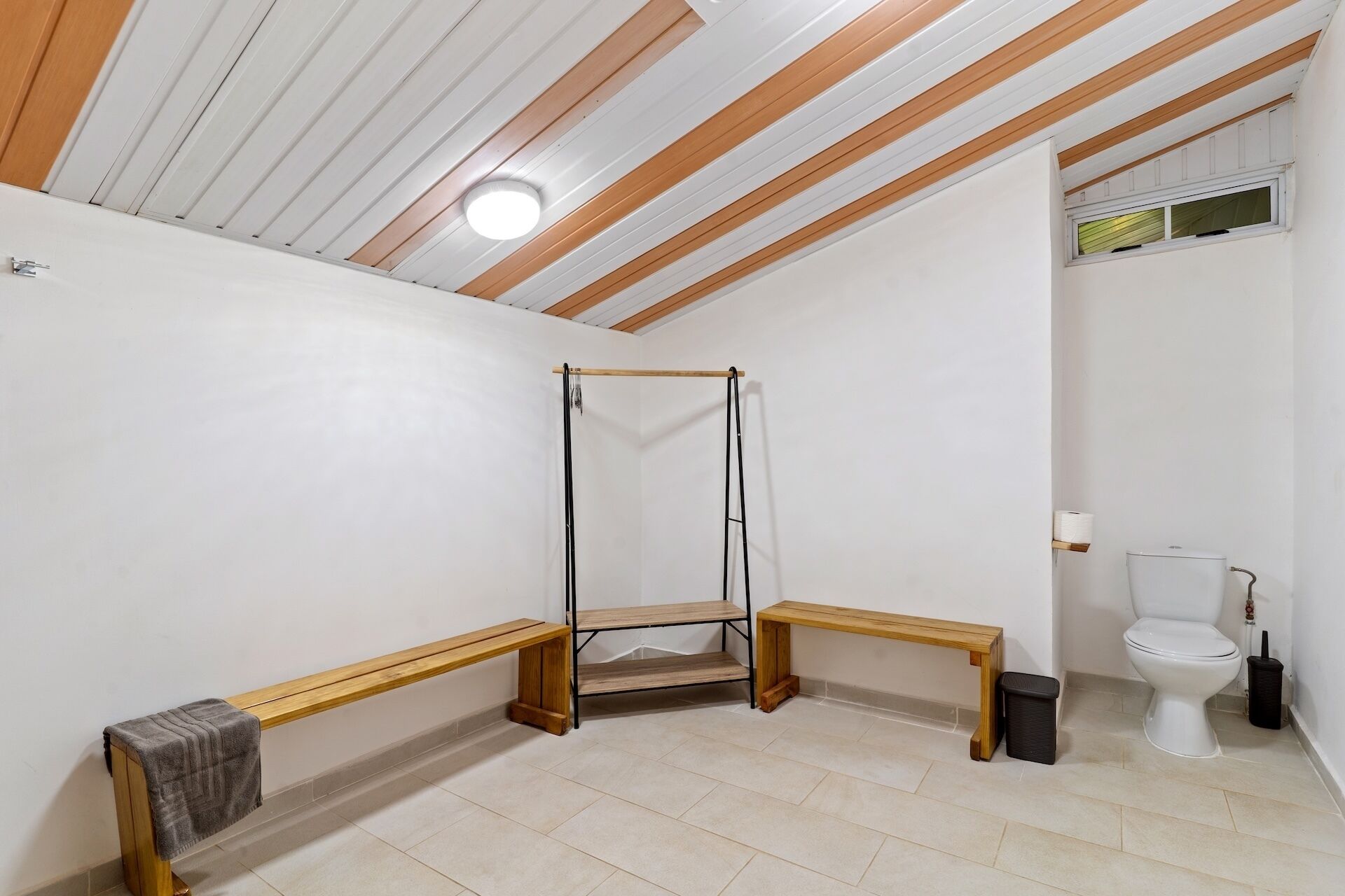 A bathroom with a wooden bench, a hanging shower, and a toilet.