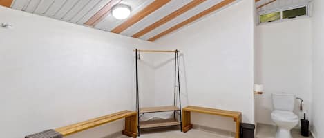 A bathroom with a wooden bench, a hanging shower, and a toilet.