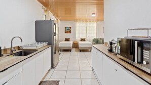 A compact kitchen with a refrigerator, microwave, and sink. There are two beds with pillows and a small seating area with a table and chairs. - Fare Manava (Tiahura)