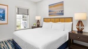 Une chambre d’hôtel avec un grand lit, deux tables de chevet avec des lampes, une fenêtre donnant sur un beau paysage et un tableau au mur.