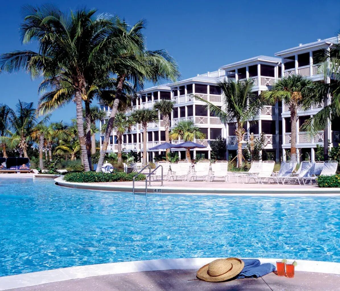 A hotel with a pool, palm trees, and lounge chairs.