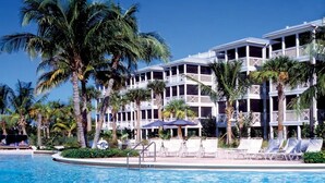 Un hôtel doté d’une piscine, de palmiers et de chaises longues.