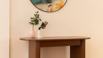 Un miroir rond accroché au mur, une petite table sur laquelle sont posés deux vases, et un luminaire suspendu.