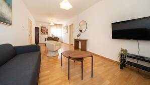 Ein modernes Wohnzimmer mit einer Couch, einem Esstisch, einem Fernseher und einem Spiegel.