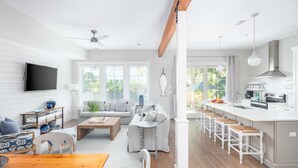 Ein modernes Wohnzimmer mit Esstisch aus Holz, einer Couch und einer Küchenzeile mit Barhocker.