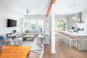 Ein modernes Wohnzimmer mit Esstisch aus Holz, einer Couch und einer Küchenzeile mit Barhocker.