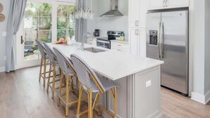 Una cocina moderna con una isla central, taburetes de bar, un refrigerador de acero inoxidable y un ventanal grande.