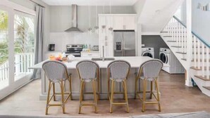 Una cocina moderna con una isla central, taburetes de bar, horno empotrado y lavadora.