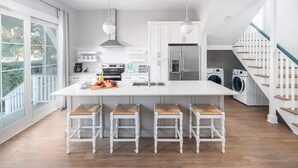 Una cocina moderna con una isla grande, taburetes de bar, horno empotrado y refrigerador.