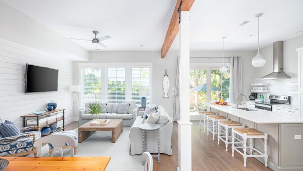 Una sala de estar moderna con una mesa de comedor de madera, un sofá y una zona de cocina con taburetes de bar.