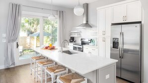 Cocina moderna con una isla central, taburetes de bar, electrodomésticos de acero inoxidable y vistas al exterior.