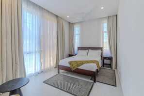 A bedroom with a bed, nightstands, a chair, and a window with curtains. - 2 or 3 Bedroom - A&E Residence  (Kwale County)