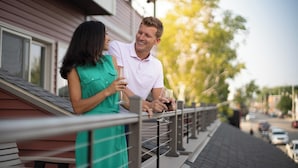A couple standing on a balcony with a railing, holding wine glasses.