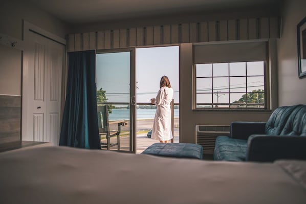 A hotel room with a bed, a view of the sea, and a balcony with a person standing.