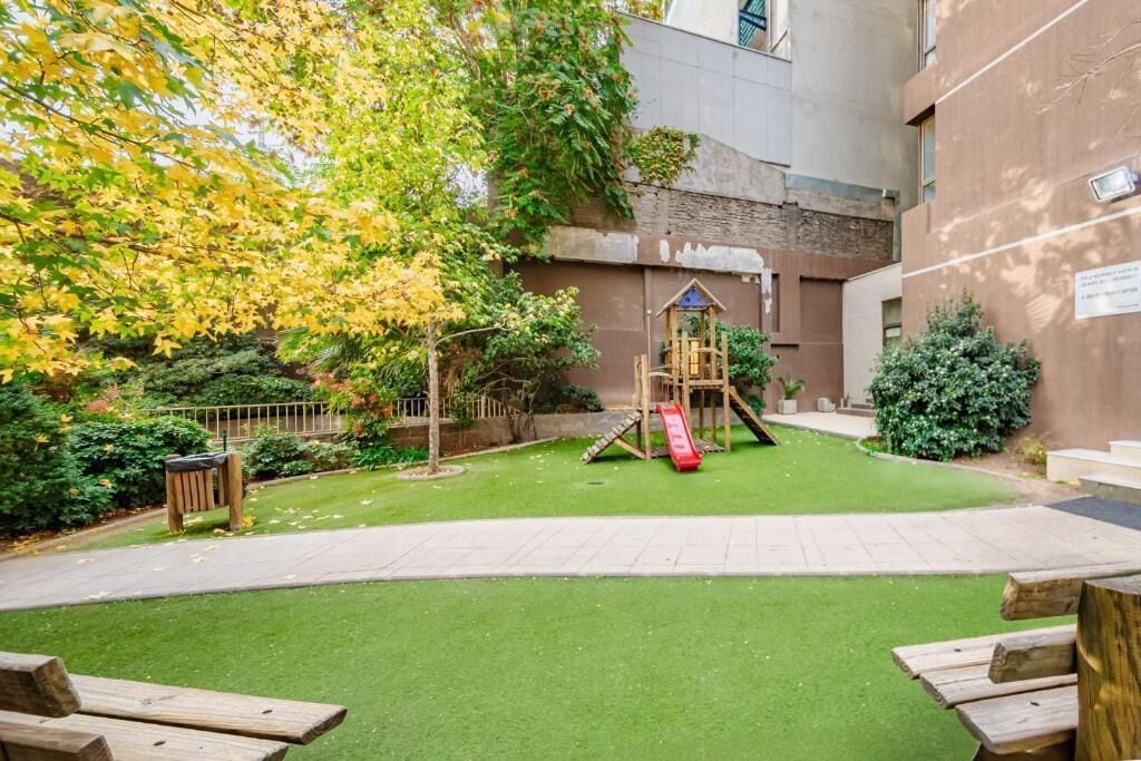 A playground with a slide and climbing structure, surrounded by a well-maintained lawn and a building in the background.