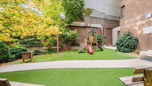 A playground with a slide and climbing structure, surrounded by a well-maintained lawn and a building in the background. - Rbk Moderno dpto ubicación inmejorable (Santiago)