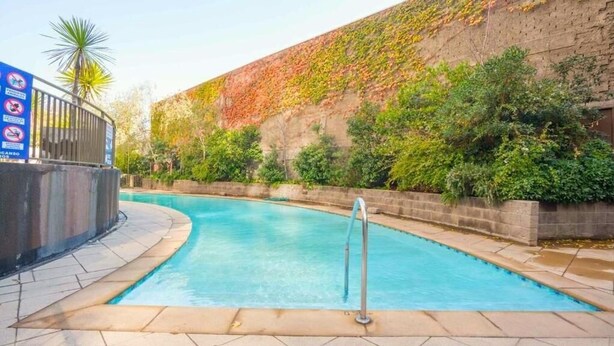 A swimming pool with a metal railing, surrounded by a brick wall with greenery. - Rbk Moderno dpto ubicación inmejorable (Santiago)