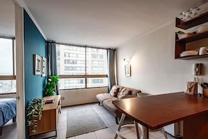 Ein modernes Wohnzimmer mit einer Couch, einem Esstisch, einer Pflanze und einem großen Fenster mit Blick auf die Stadt.