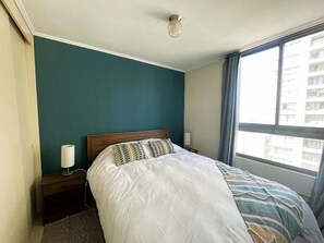 Ein Schlafzimmer mit einem Bett, einem Nachttisch, einer Lampe und einem Fenster mit Vorhängen.