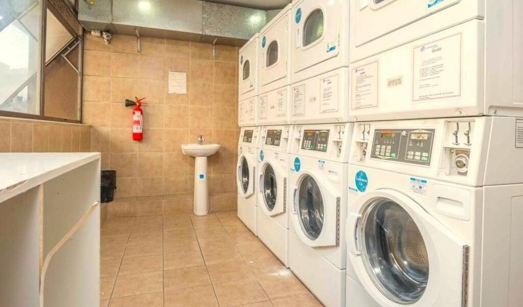 A laundry room with multiple stacked washing machines, a sink, and a fire extinguisher.