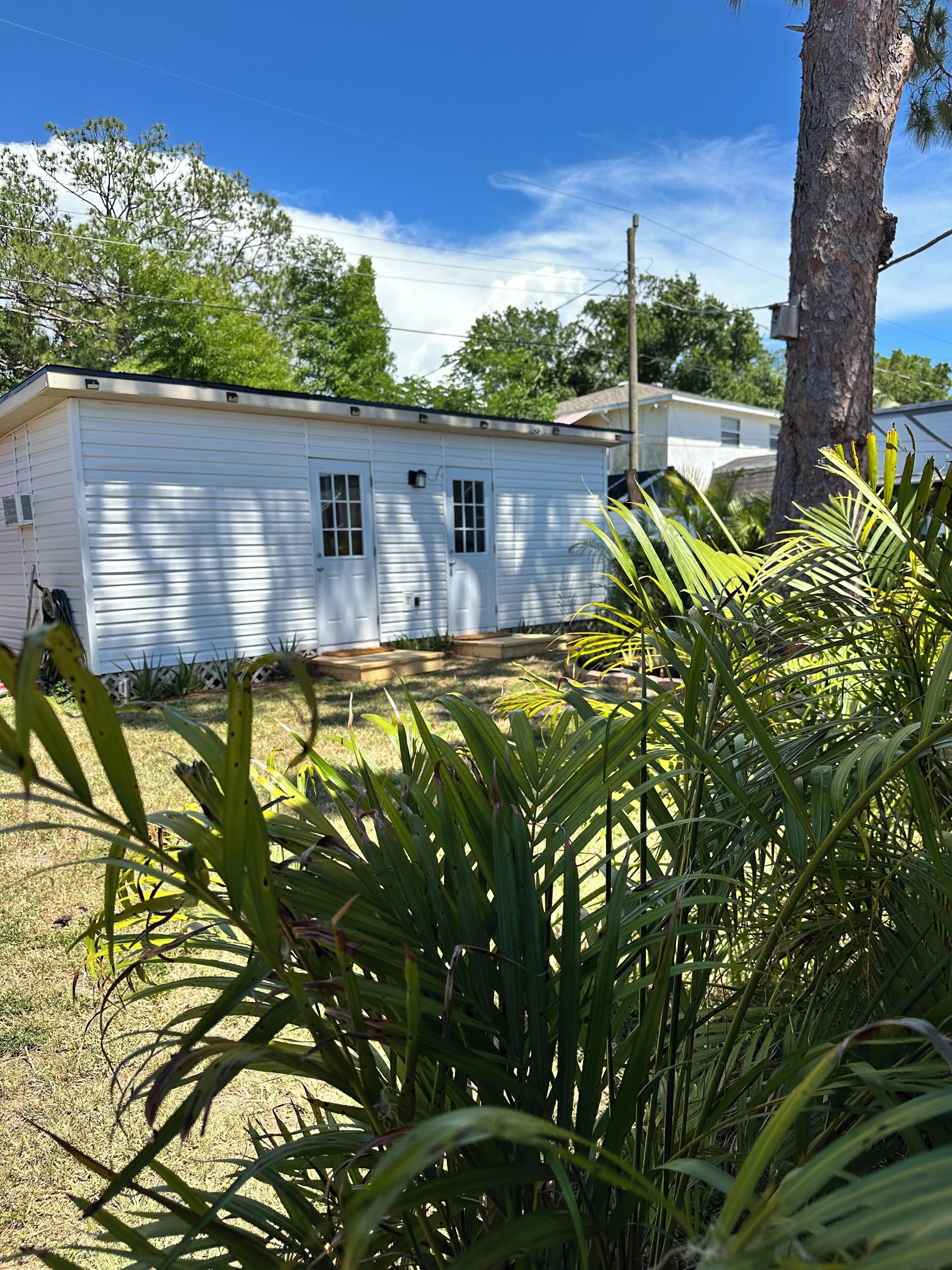 Una casa móvil de un piso con techo plano, un porche delantero y un pequeño jardín con césped y una palmera.