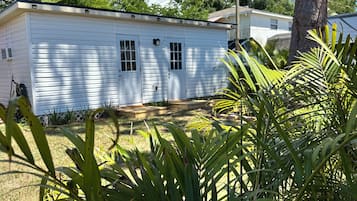 Una casa móvil de un piso con techo plano, un porche delantero y un pequeño jardín con césped y una palmera.
