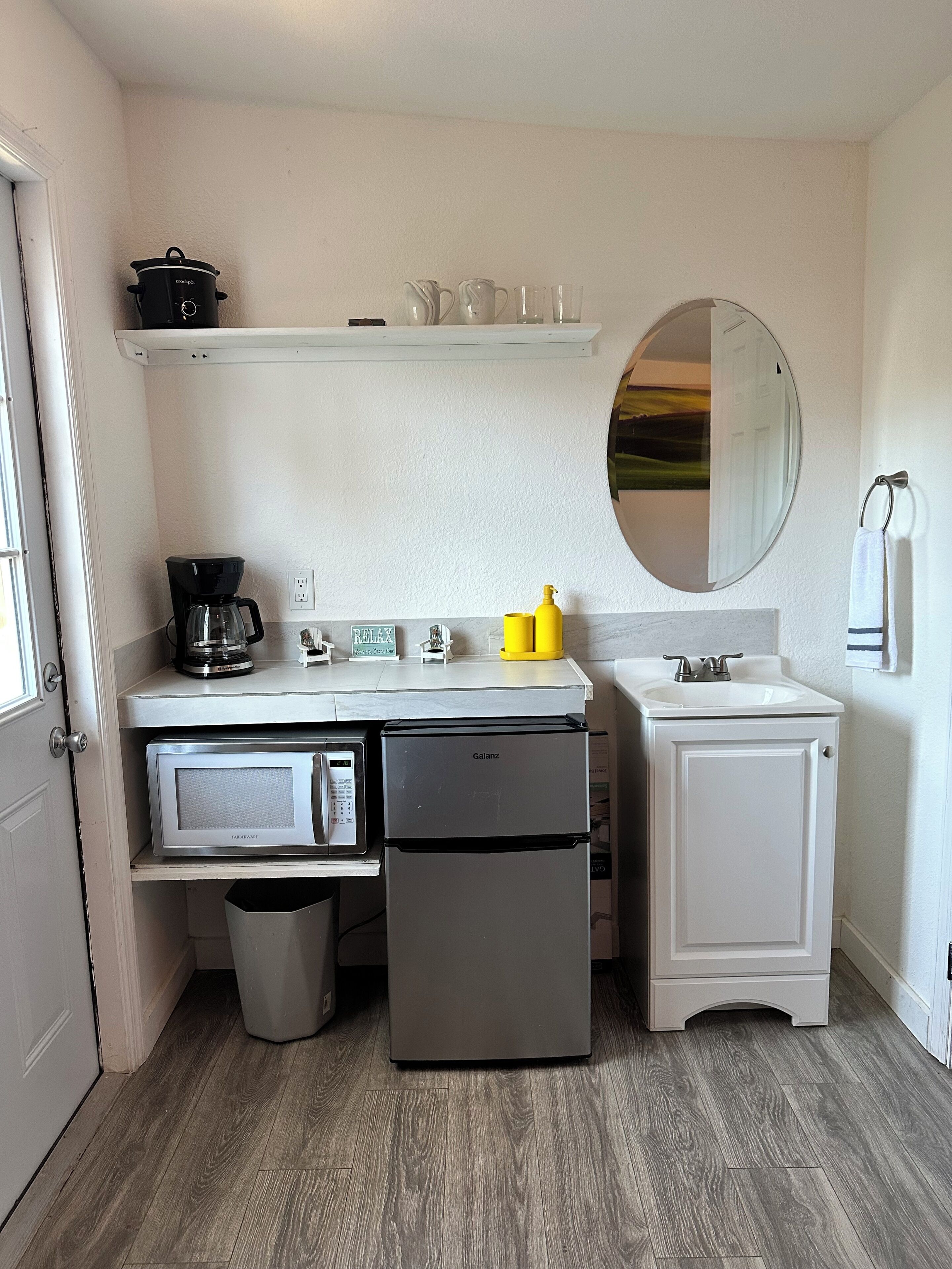 Una kitchenette compacta con microondas, refrigerador Galanz, cafetera y un lavamanos pequeño.