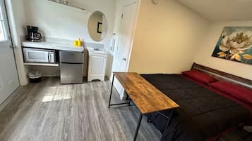 A compact room with a bed, a desk, and a kitchenette.