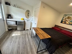 Habitación compacta con cama, escritorio y kitchenette.