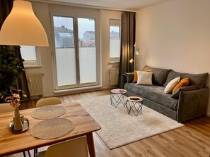 Een moderne woonkamer met een bank, een eettafel met placemats, een lamp en uitzicht door grote ramen.
