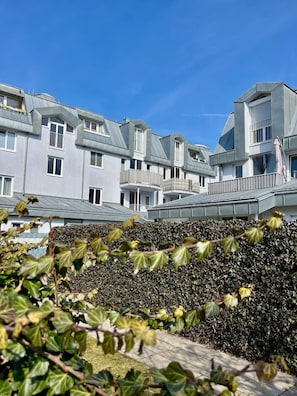 Een modern gebouw met meerdere balkons en een haag op de voorgrond.