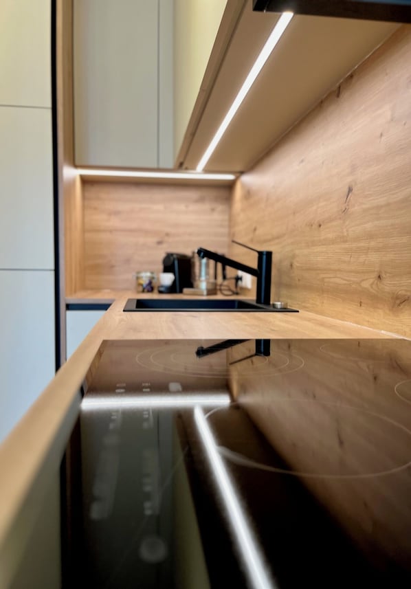 Une cuisine moderne dotée d’un plan de travail en bois, d’appareils électroménagers en acier inoxydable et d’un robinet noir.