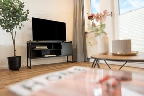 Un salon moderne avec un téléviseur à écran plat, une bibliothèque, une plante en pot et une petite table sur laquelle est posée une bougie.