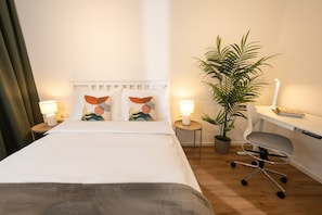 Un lit bien fait, avec des oreillers, une lampe de chevet, un bureau avec une chaise et une plante en pot.