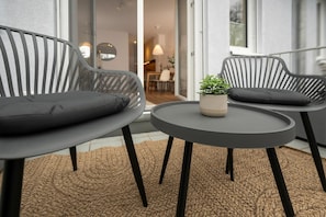 Een moderne buitenzitplaats met twee stoelen en een kleine tafel, een plant in pot en uitzicht op het gebouw.
