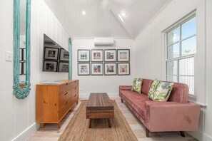A living room with a wooden dresser, a red sofa with patterned cushions, a coffee table, and framed pictures on the wall. - Retro Designer Bungalow 200' from Beach w/ VW Bus Grill & Pool (Harbour Island)