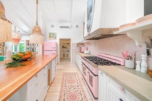 Een keuken met een centraal eiland, een roze kookplaat en een hanglamp.