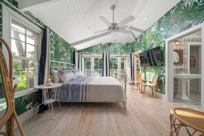 Un dormitorio con cama, ventilador de techo, televisor y vistas al exterior.