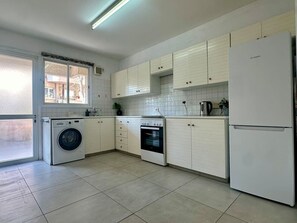 Eine Küche mit Waschmaschine, Backofen, Kühlschrank und Schränken.