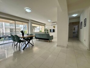 A spacious living area with a sofa, dining table, chairs, and a TV.