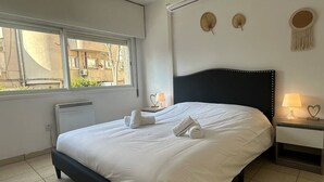 A neatly made bed with white linens and towels, a bedside table with a lamp, and a window with a view of buildings outside. - 2 bedrooms flat near center (Egkomi)