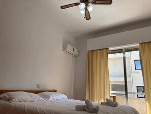 Une chambre d’hôtel avec un lit, un ventilateur de plafond, un appareil de climatisation et une fenêtre avec des rideaux.