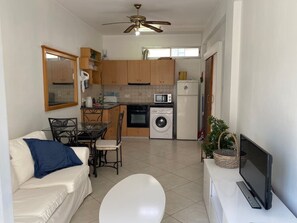 Un espace de vie compact comprenant un coin repas, une kitchenette et un téléviseur posé sur un meuble.