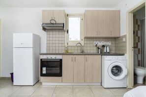 A compact kitchen with a refrigerator, oven, washing machine, and a window above the sink. - Renovated city center studio balcony/terrace view (Nicosia)
