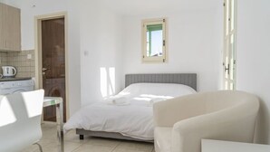 A bedroom with a bed, a chair, a table, and a window. - Renovated city center studio balcony/terrace view (Nicosia)
