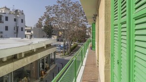 Un balcon avec des volets verts donnant sur une rue bordée de voitures garées et d’immeubles.