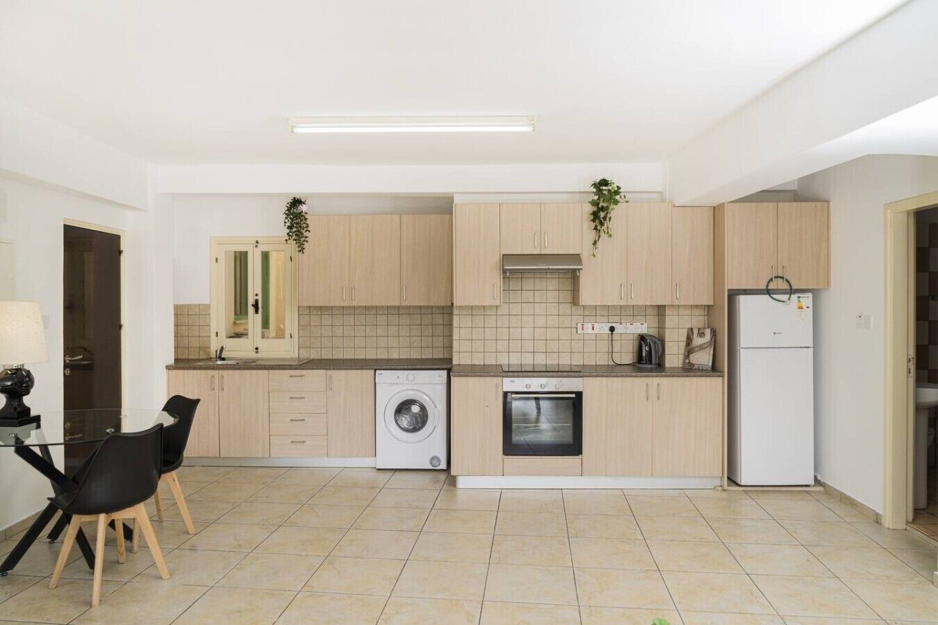 A modern kitchen with light wood cabinets, a built-in washing machine, an oven, and a refrigerator.
