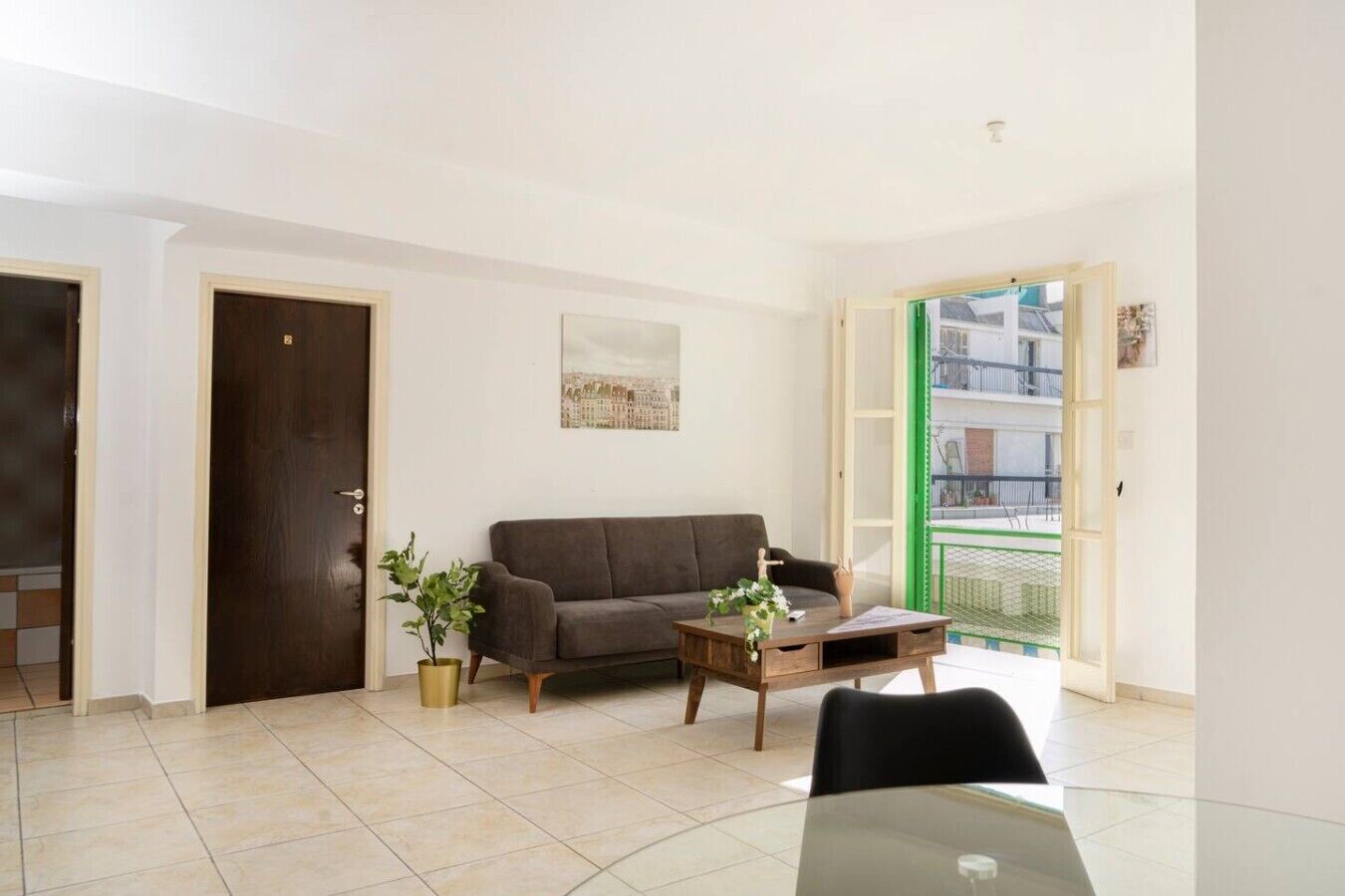 Una sala de estar con un sofá, una mesa de centro, una planta en maceta y vistas a través de una puerta.